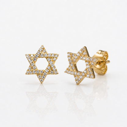 A pair of gold Star of David stud earrings paved with small diamonds, displayed on a clean white reflective surface.