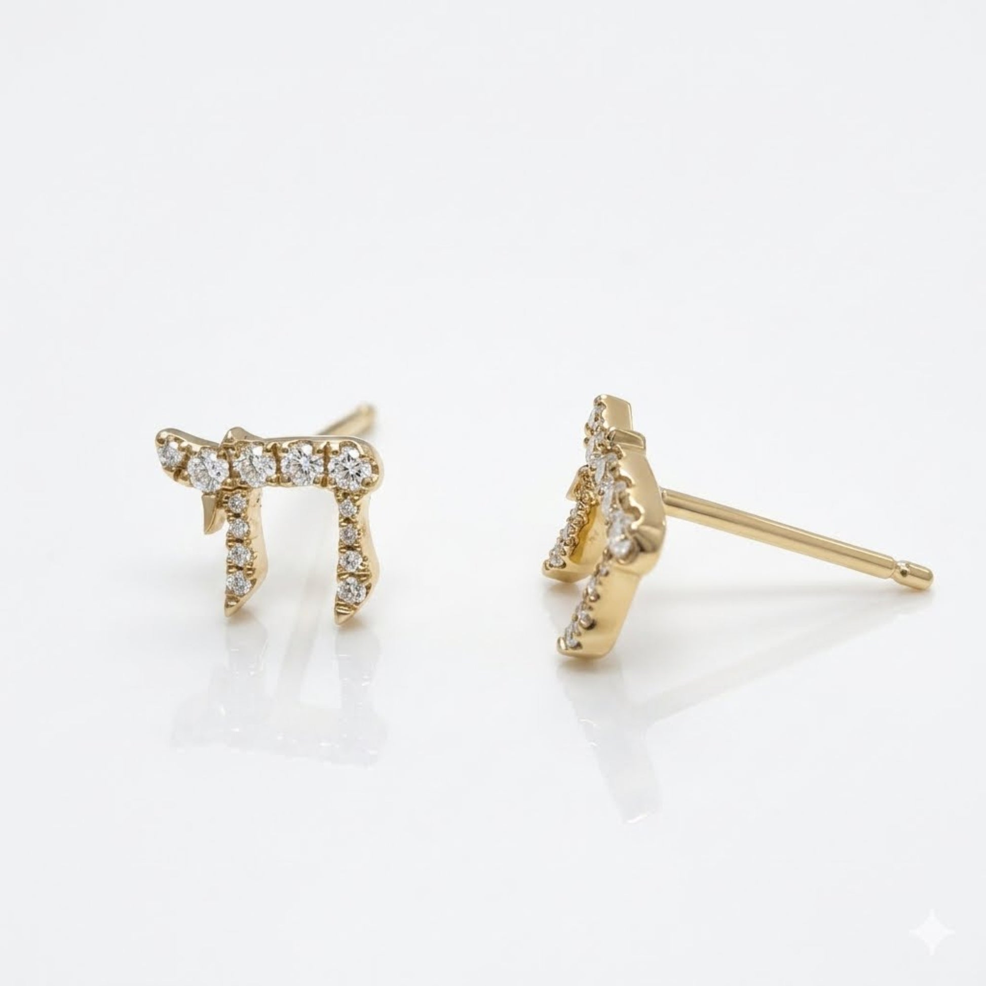 A pair of gold-tone stud earrings featuring a stylized Hebrew letter 'Shin' embellished with small clear pavé stones, shown on a clean white reflective surface.