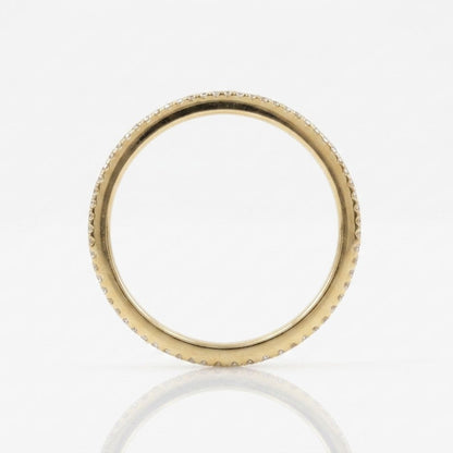 A thin yellow gold ring with a textured, beaded outer edge and a smooth inner band, shown on a reflective white surface.