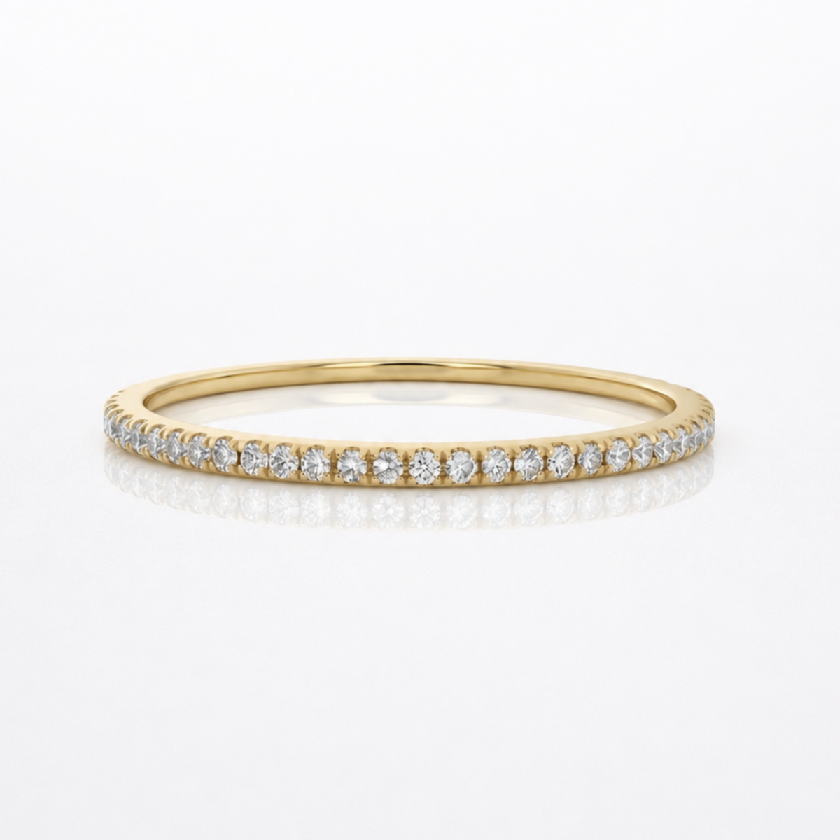 A delicate yellow gold eternity ring set with small round diamonds, shown on a clean white background with a soft reflection.