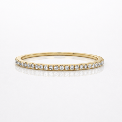 A delicate yellow gold eternity ring set with small round diamonds, shown on a clean white background with a soft reflection.