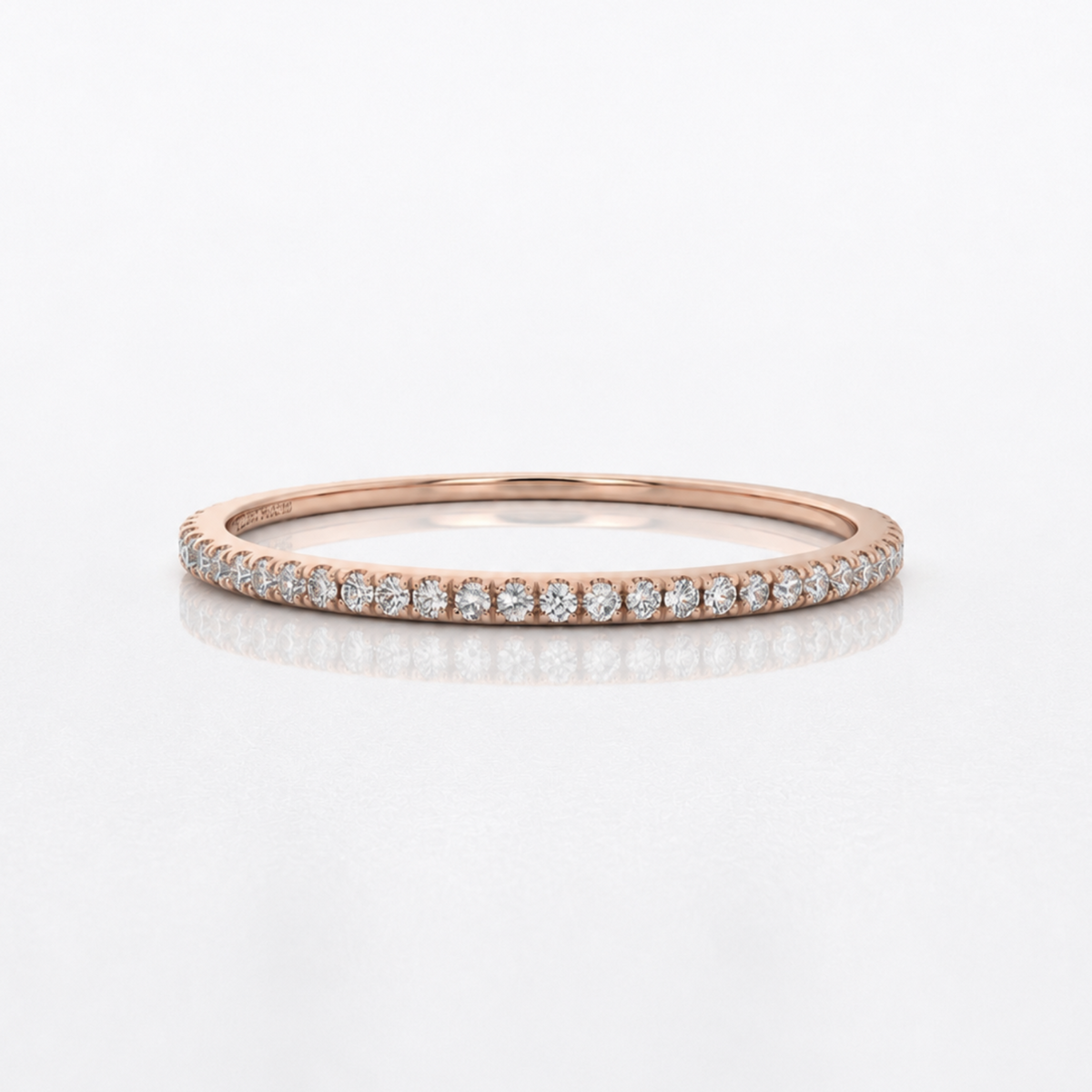 A rose gold eternity ring set with small round diamonds, shown on a clean white reflective surface.