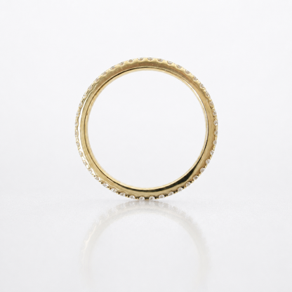 A gold eternity ring with a textured beaded outer edge, photographed from above on a clean white reflective surface.