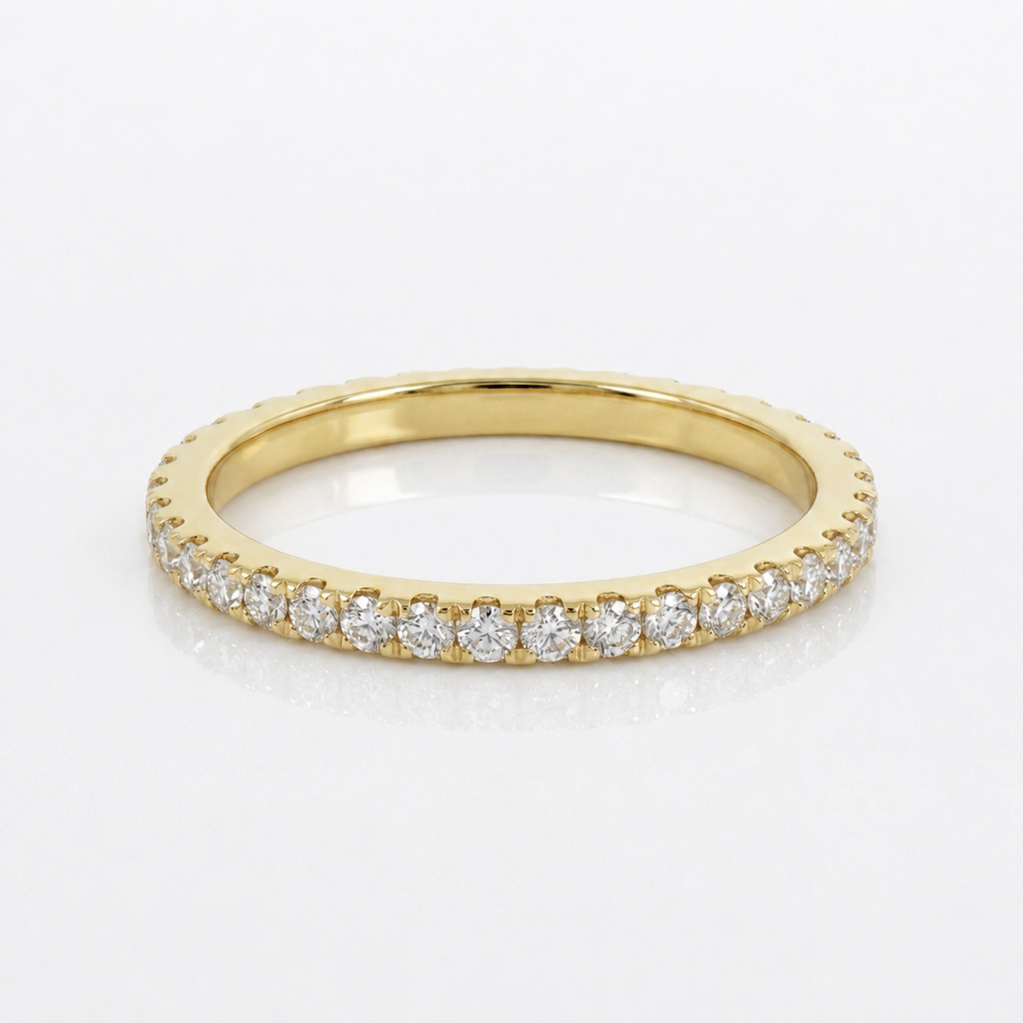 A yellow gold eternity ring featuring a continuous row of round-cut clear diamonds in a prong setting, displayed on a clean white reflective surface.