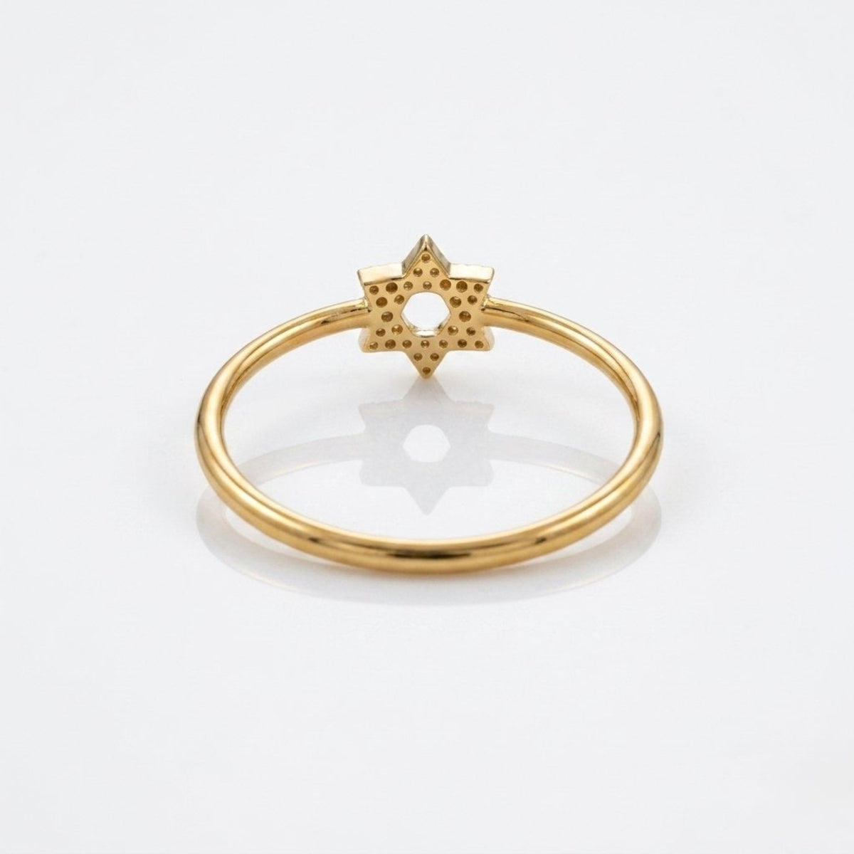 A gold ring featuring a textured six-pointed star charm with tiny inset stones, photographed on a clean white background with a soft reflection.