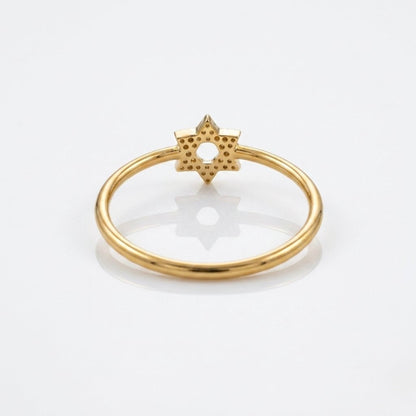 A gold ring featuring a textured six-pointed star charm with tiny inset stones, photographed on a clean white background with a soft reflection.