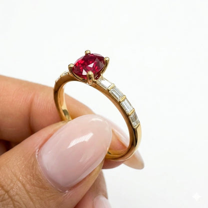 A gold ring with a marquise-cut red ruby and baguette-cut diamonds  on the band, held between fingers against a white background.