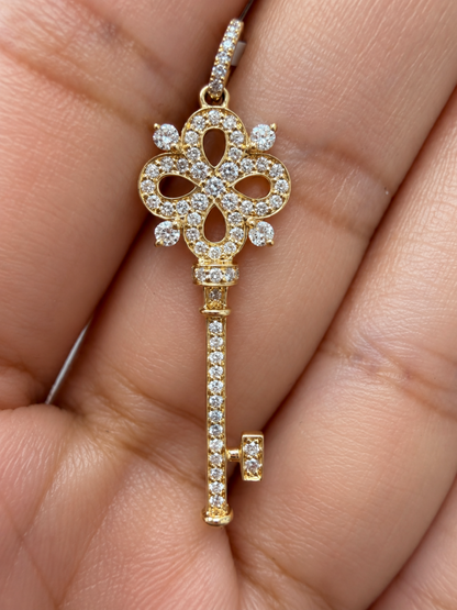 A gold key-shaped pendant encrusted with diamonds, held in the palm of a hand.