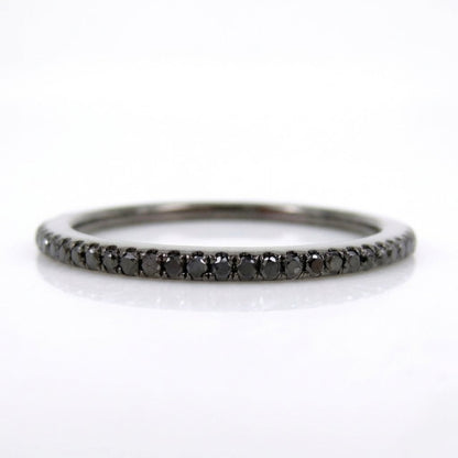 A slim black diamond eternity band ring set in a polished silver-toned metal, shown on a clean white background with a soft reflection.