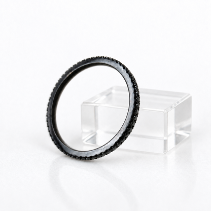 A circular black camera lens filter with a textured outer rim, displayed leaning against a clear acrylic block on a white reflective surface.