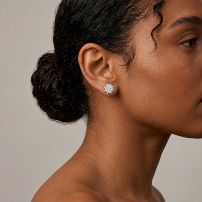 A close-up side profile of a woman wearing a small silver-toned flower-shaped stud earring against a warm beige background.