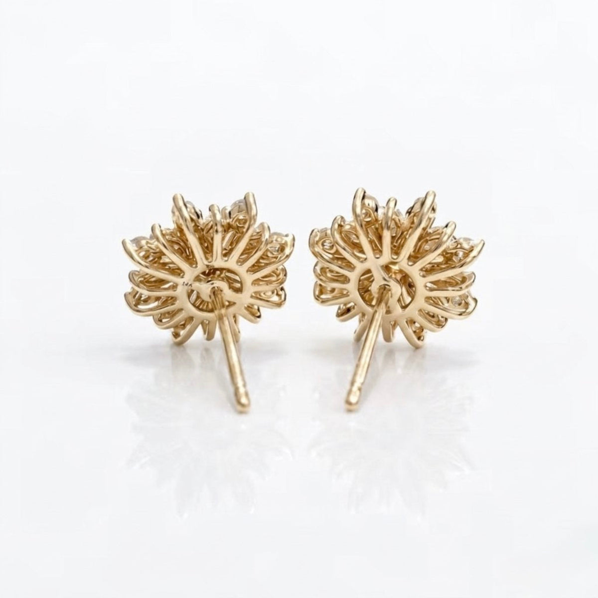 A pair of gold dandelion stud earrings with intricate petal details and post backs, displayed on a clean white reflective surface.