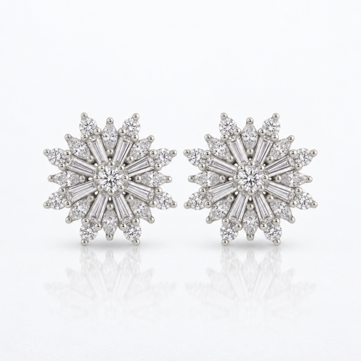A pair of snowflake-shaped diamond stud earrings in silver-toned metal, featuring a central round diamond surrounded by baguette, marquise and round-cut diamonds, set against a clean white background with a soft reflection below.