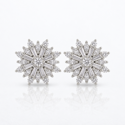 A pair of snowflake-shaped diamond stud earrings in silver-toned metal, featuring a central round diamond surrounded by baguette, marquise and round-cut diamonds, set against a clean white background with a soft reflection below.