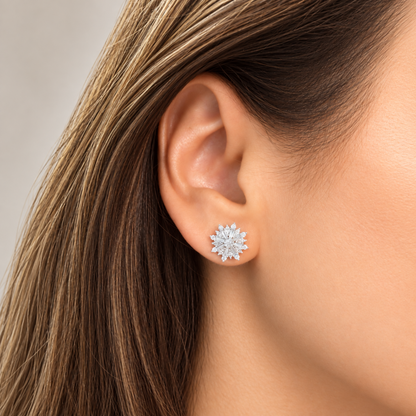 A close-up of a woman's ear wearing a small silver-toned stud earring with a snowflake or starburst cluster of clear diamonds.