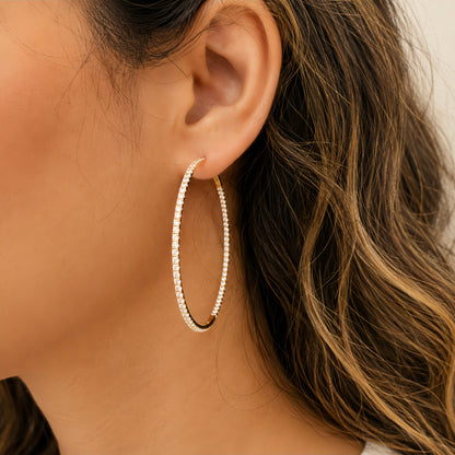 A close-up of a model's ear wearing a large, double-row hoop earring made of small clear diamonds in a gold-tone setting.