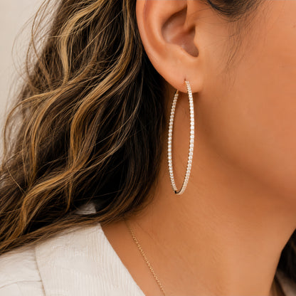 A close-up of a woman wearing a large silver hoop earring adorned with small clear diamonds, shown against her ear, hair, and neck.