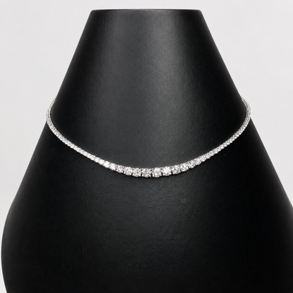 A delicate silver tennis necklace with clear diamonds, displayed on a black jewelry bust against a light gray background.