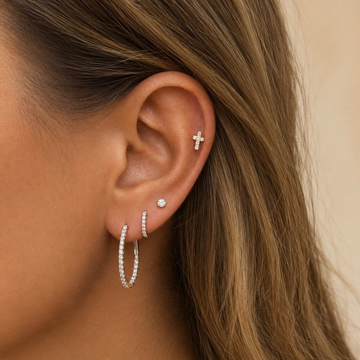 Natural diamond cross stud earring worn with other earrings on ear