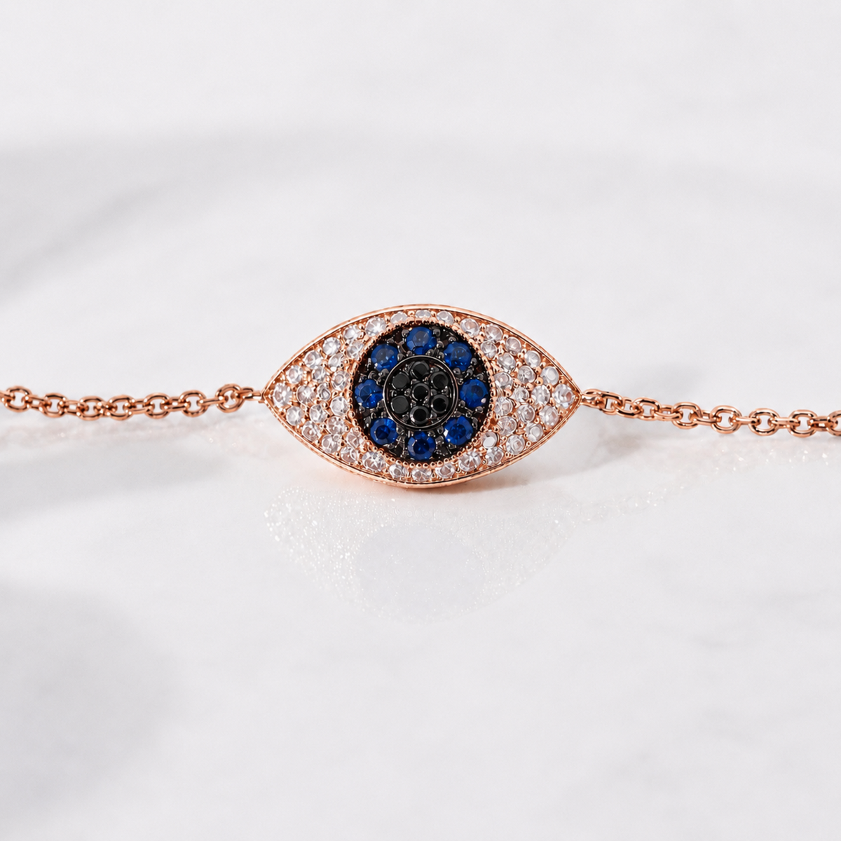 A rose gold evil eye bracelet featuring a central blue and black evil eye motif surrounded by pavé-set clear diamonds, displayed on a white marble surface.