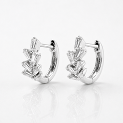A pair of silver huggie hoop earrings with baguette-cut clear gemstones, displayed on a clean white reflective surface.