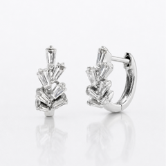 A pair of silver huggie hoop earrings with a cluster of baguette-cut clear diamonds, displayed on a clean white reflective surface.