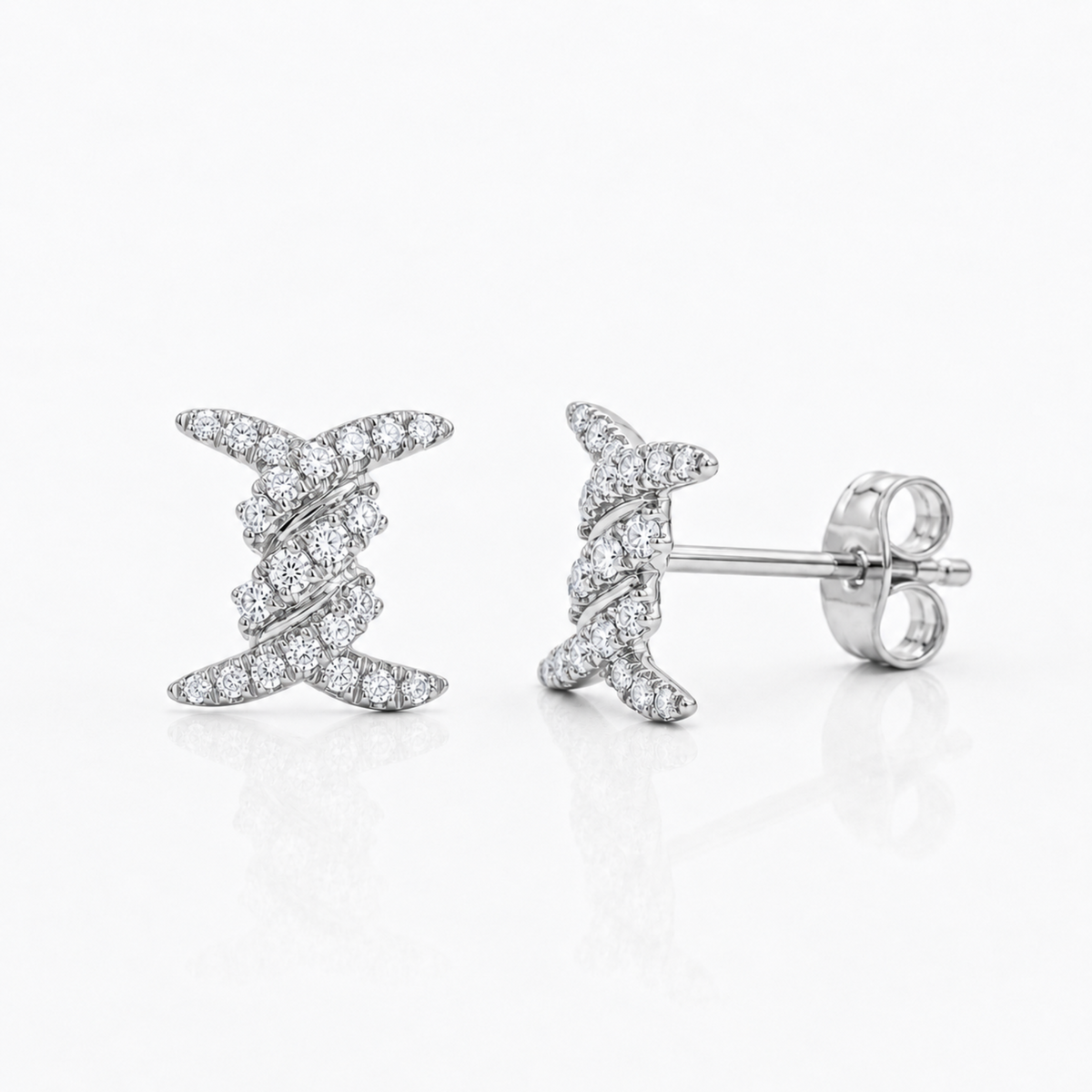A pair of silver-toned stud earrings with a twisted, ribbon-like design paved with small diamonds stones, shown on a clean white background. One earring is facing forward, and the other is turned to show the post and butterfly back.
