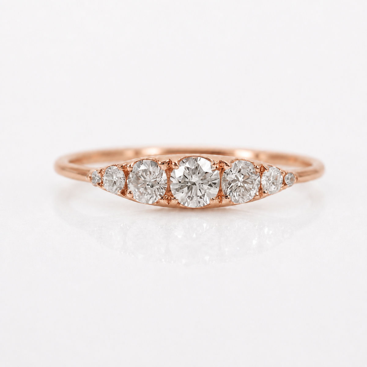 A rose gold diamond ring with a marquise-shaped arrangement of five diamonds, set against a clean white background with a soft reflection.