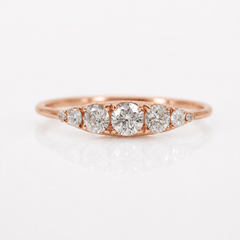 A rose gold diamond ring with a marquise-shaped arrangement of five diamonds, set against a clean white background with a soft reflection.