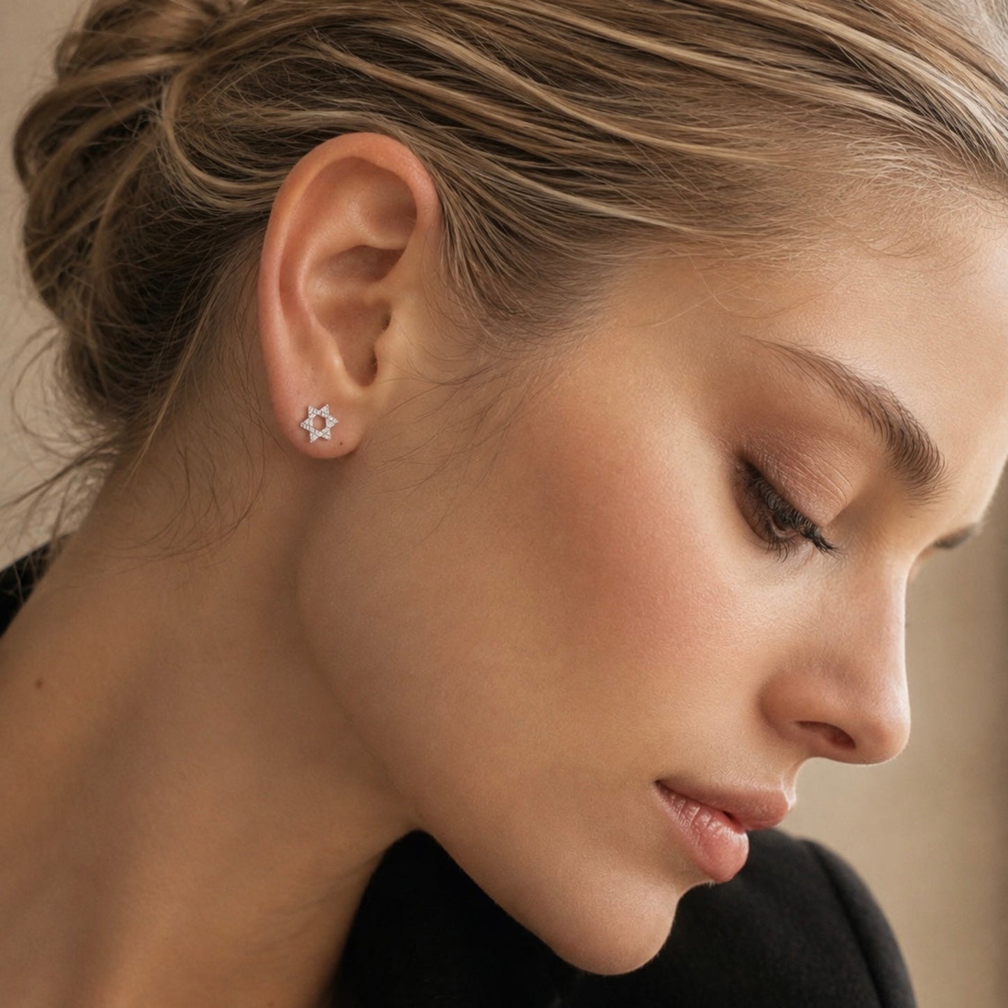 A close-up of a woman wearing a small silver star-shaped stud earring on her earlobe.