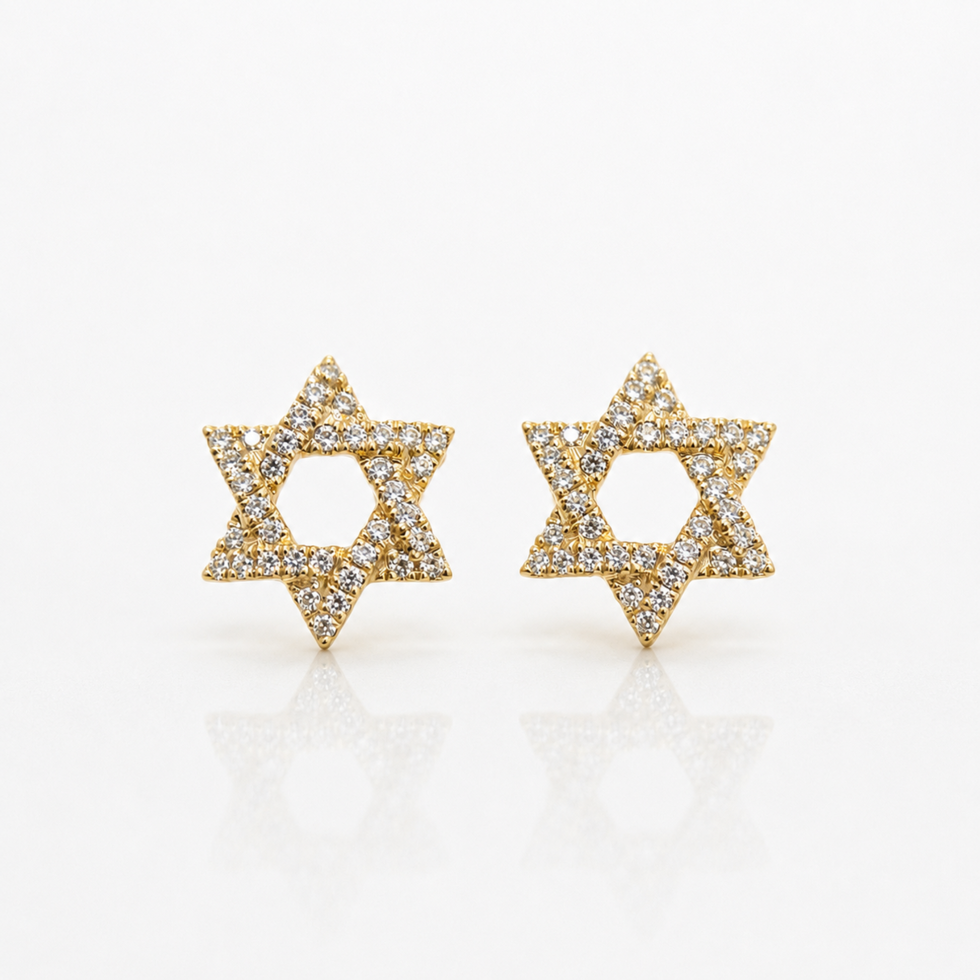 A pair of gold Star of David stud earrings paved with small clear diamonds, displayed on a clean white reflective surface.