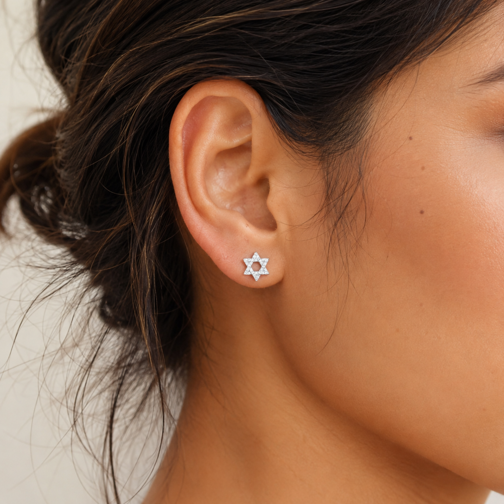 A close-up of a woman's ear wearing a small silver Star of David stud earring.