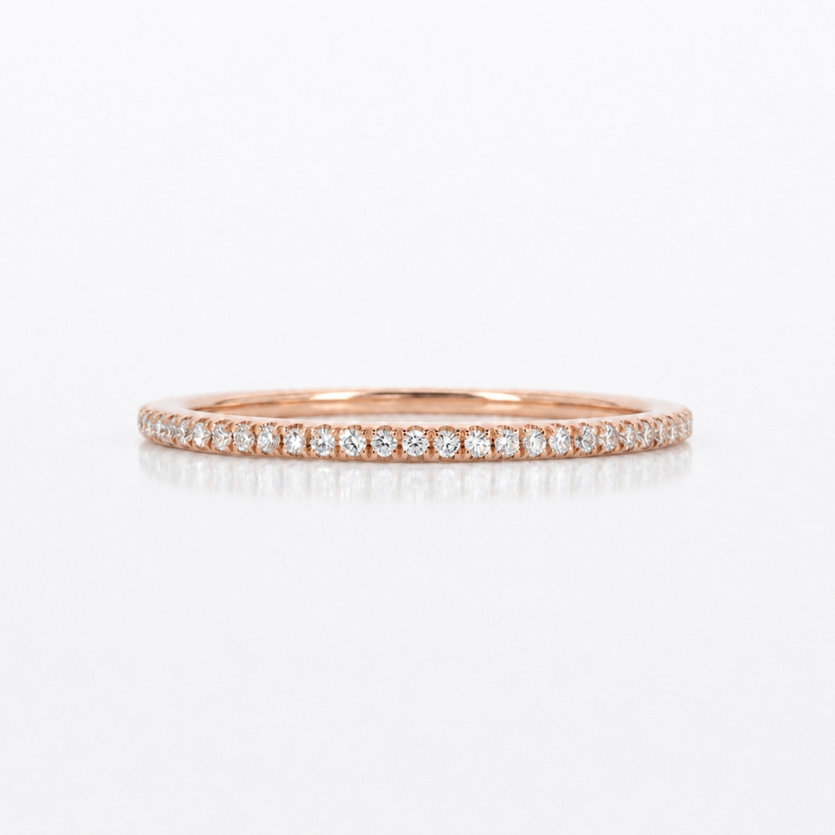 A thin rose gold eternity ring paved with small round-cut diamonds, shown on a clean white background with a soft reflection.