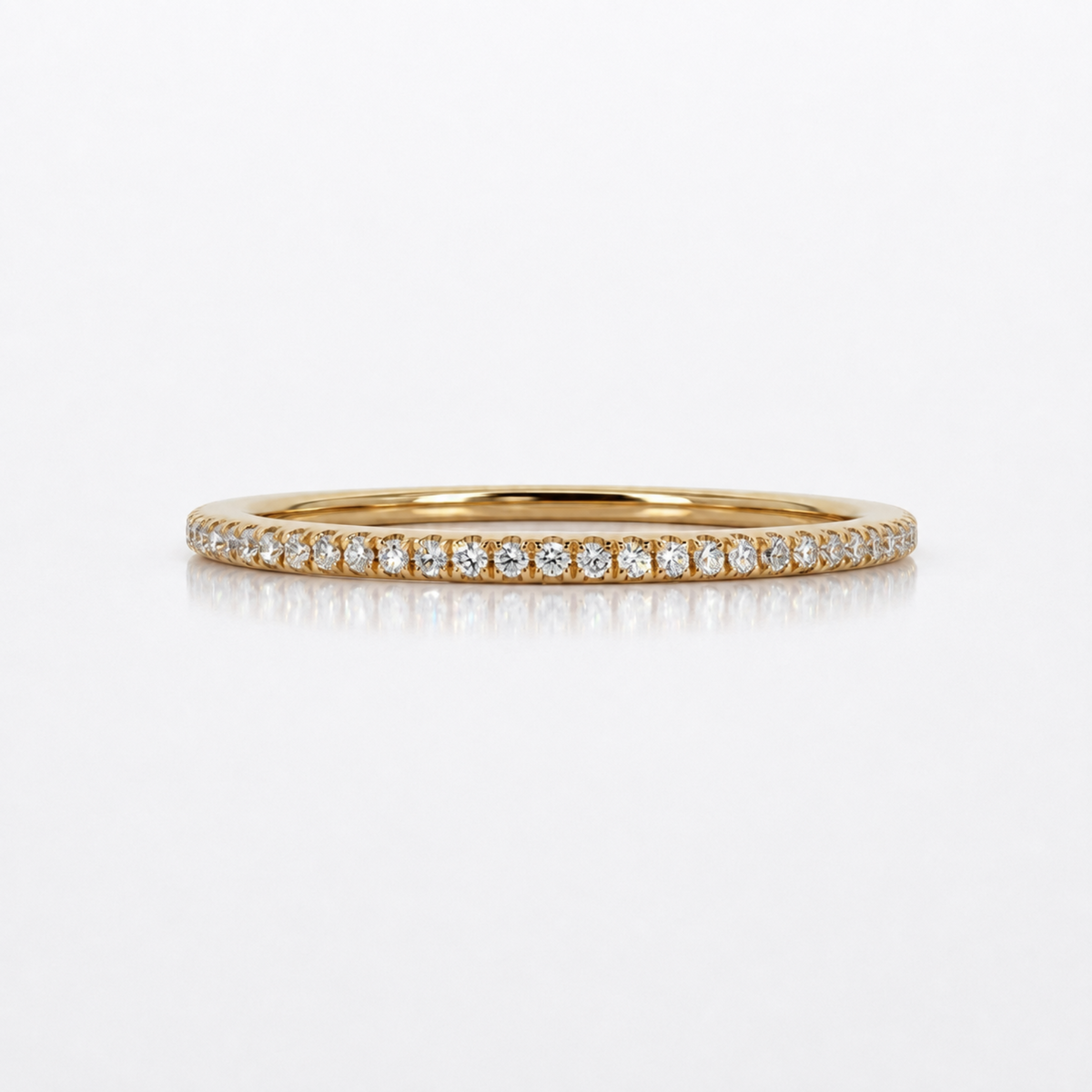 A thin yellow gold eternity ring paved with small round-cut diamonds, displayed on a clean white reflective surface.