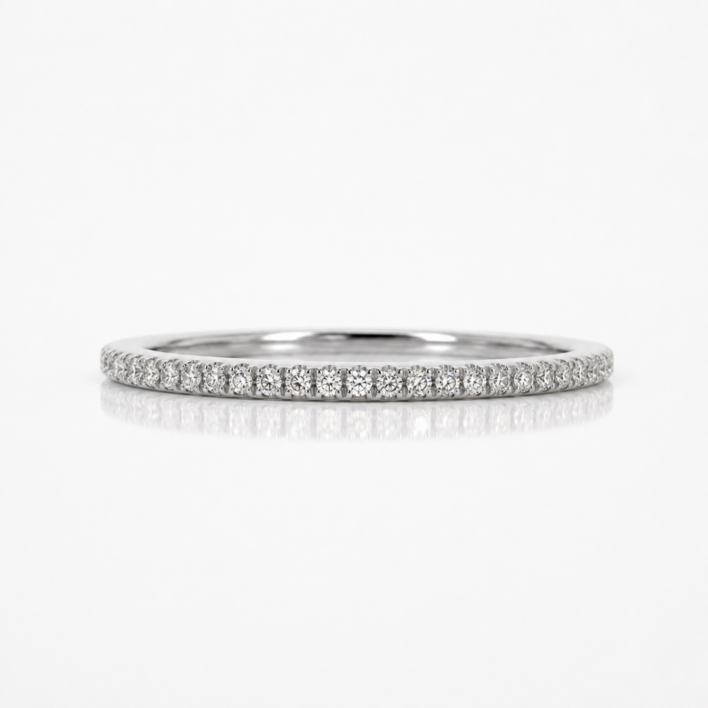A thin diamond eternity band ring in silver-colored metal, featuring a continuous row of small round-cut diamonds set in a pave style, shown on a clean white background with a soft reflection below.
