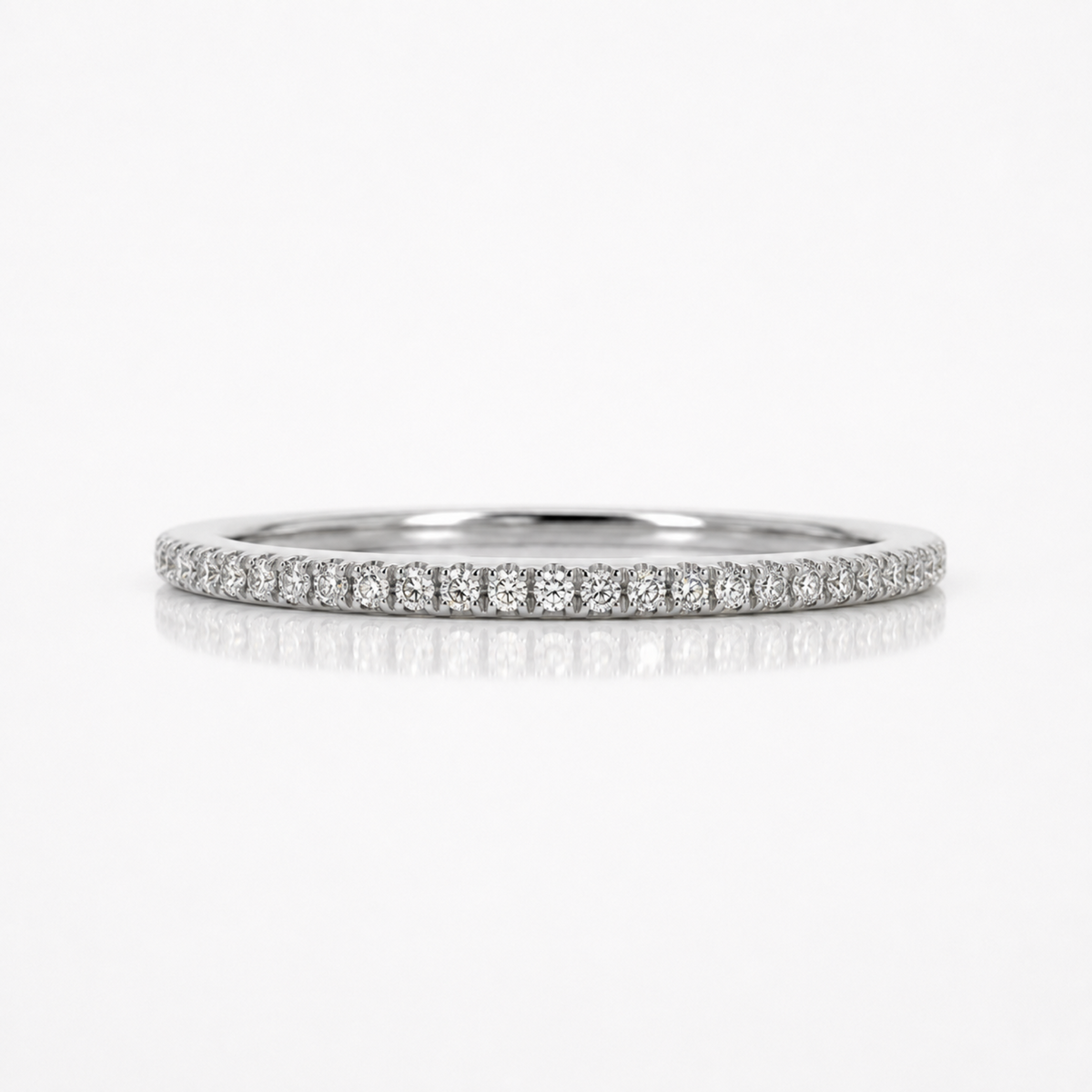 A thin diamond eternity band ring in silver-colored metal, featuring a continuous row of small round-cut diamonds set in a pave style, shown on a clean white background with a soft reflection below.
