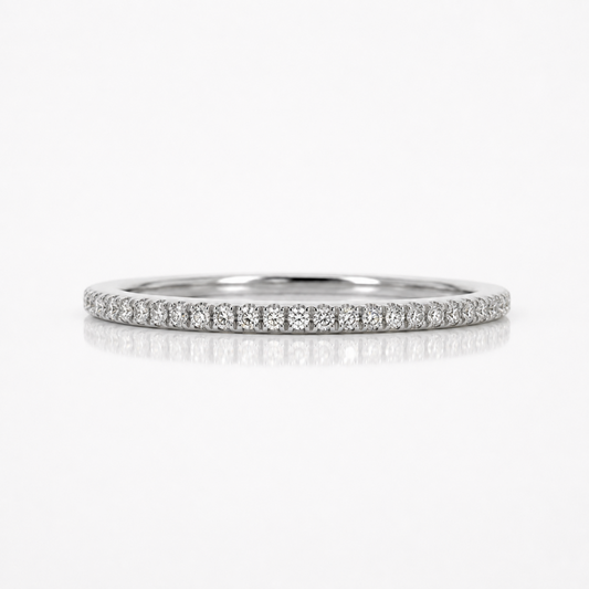 A thin diamond eternity band ring in silver-colored metal, featuring a continuous row of small round-cut diamonds set in a pave style, shown on a clean white background with a soft reflection below.