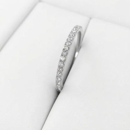 A silver-tone eternity ring set with small clear round diamonds, displayed on a white cushion inside a jewelry box.