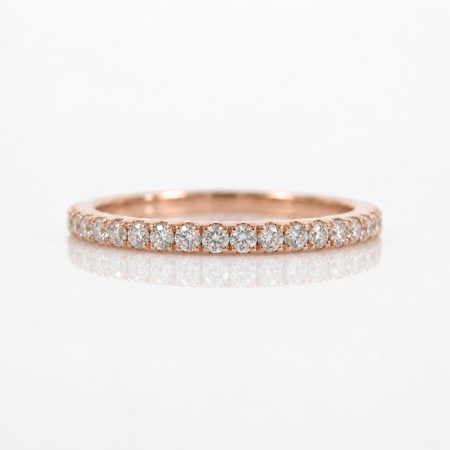 A rose gold eternity ring featuring a row of round-cut diamonds set in a polished band, shown on a clean white reflective surface.
