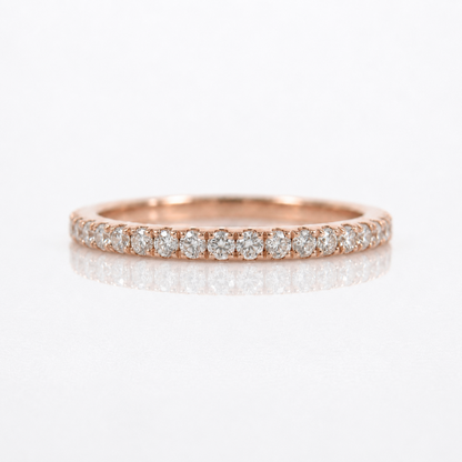 A rose gold eternity ring featuring a row of round-cut diamonds set in a polished band, shown on a clean white reflective surface.