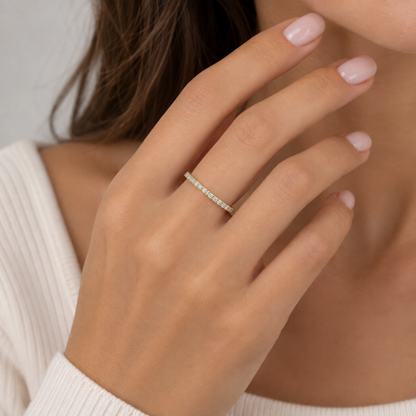 A close-up of a woman's hand wearing a delicate, thin gold band ring set with small clear diamonds, shown against her neck and shoulder.