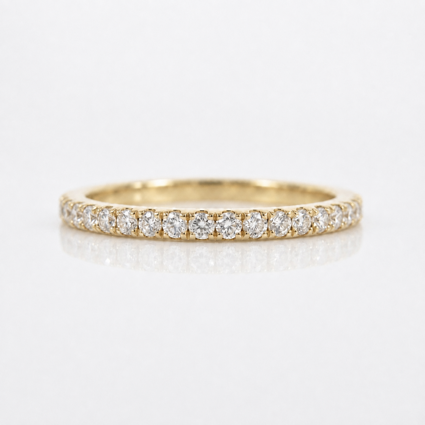 A yellow gold eternity ring set with round brilliant-cut diamonds, shown on a clean white reflective surface.