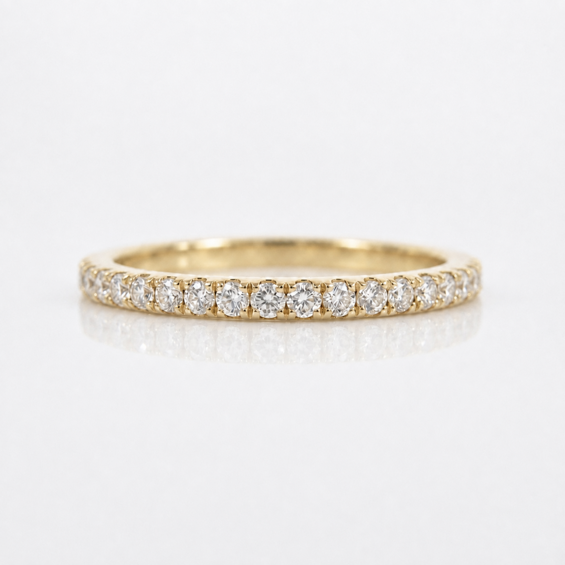 A yellow gold eternity ring set with round brilliant-cut diamonds, shown on a clean white reflective surface.