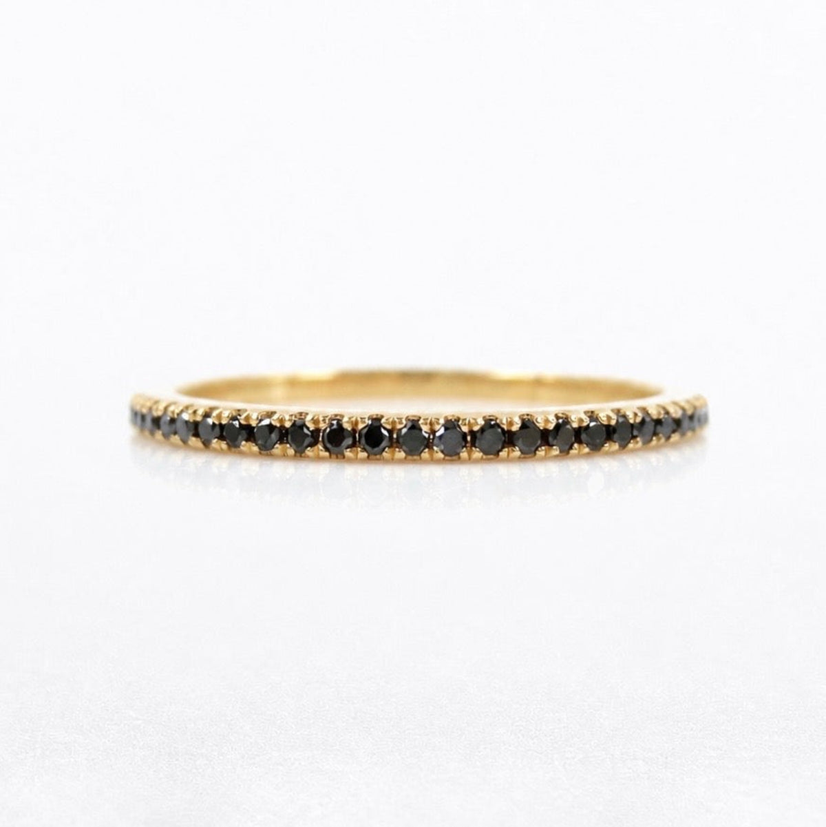 A delicate yellow gold eternity ring featuring a continuous row of small round black diamonds, shown on a clean white background.