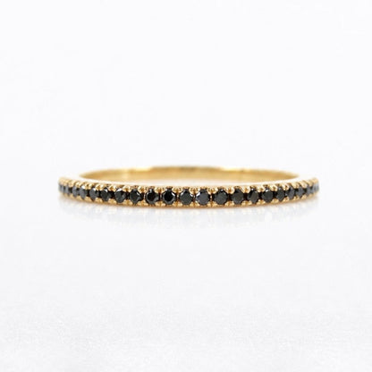 A delicate yellow gold eternity ring featuring a continuous row of small round black diamonds, shown on a clean white background.