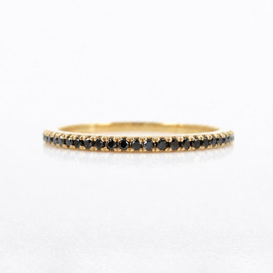 A delicate yellow gold eternity ring featuring a continuous row of small round black diamonds, shown on a clean white background.