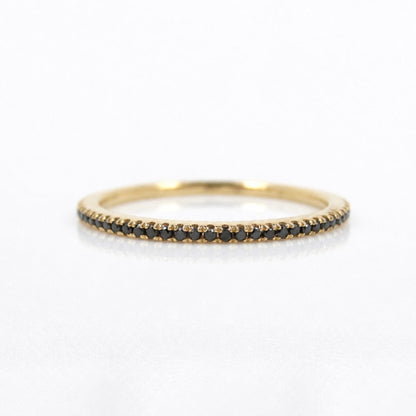 A delicate yellow gold eternity ring featuring a single row of small round black diamonds, photographed on a clean white background.
