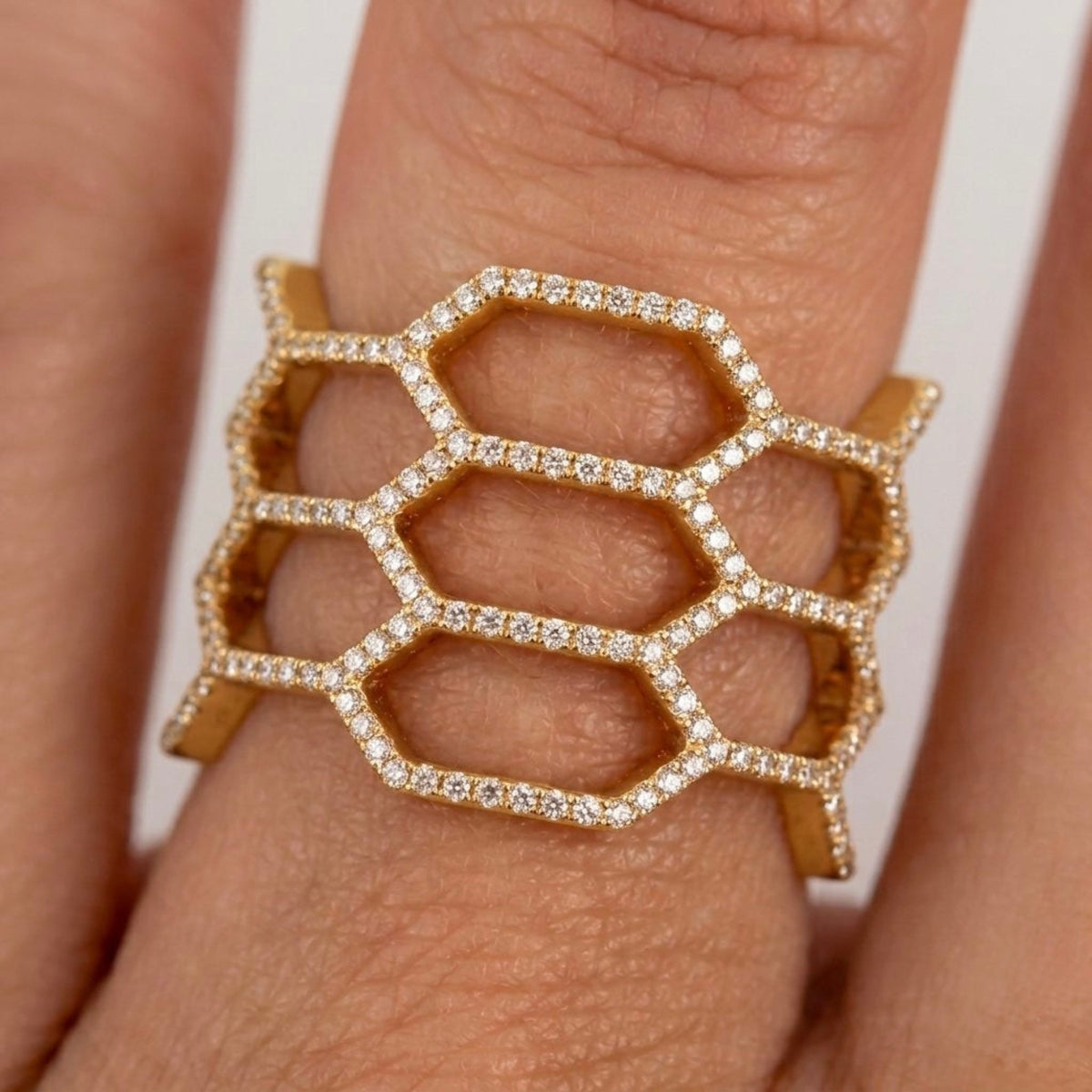 A gold ring with a wide, openwork hexagonal honeycomb design set with small diamonds, shown worn on a finger.