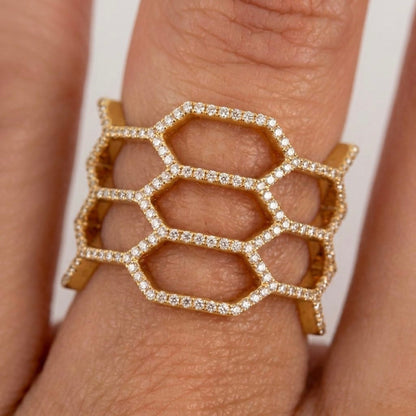A gold ring with a wide, openwork hexagonal honeycomb design set with small diamonds, shown worn on a finger.