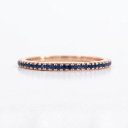 A rose gold eternity ring featuring a continuous row of round-cut deep blue sapphires, shown on a clean white background.